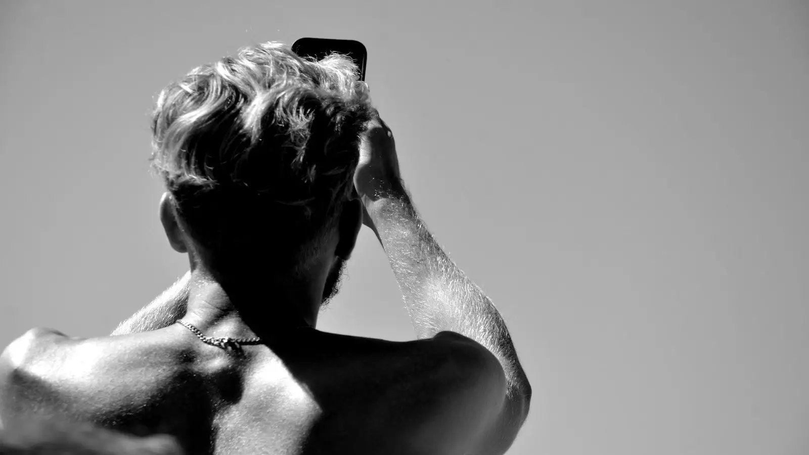 Black and white photo of a man seen from behind with one hand raised to his hair