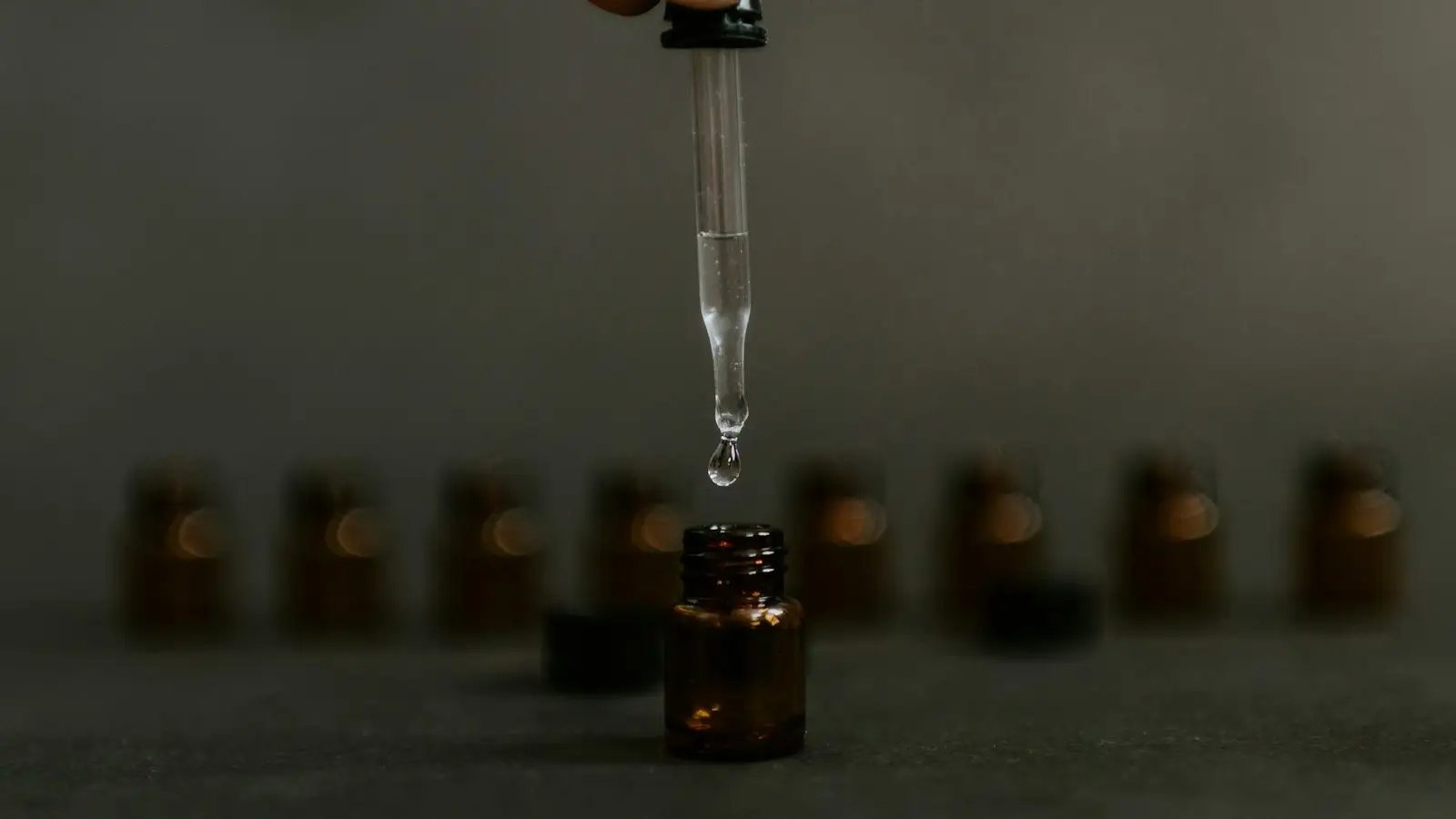 A clear drop falling from a pipette above an unlabelled amber bottle