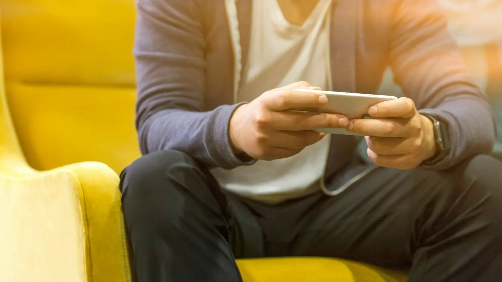 A person sitting on a yellow chair holding a smartphone in both hands